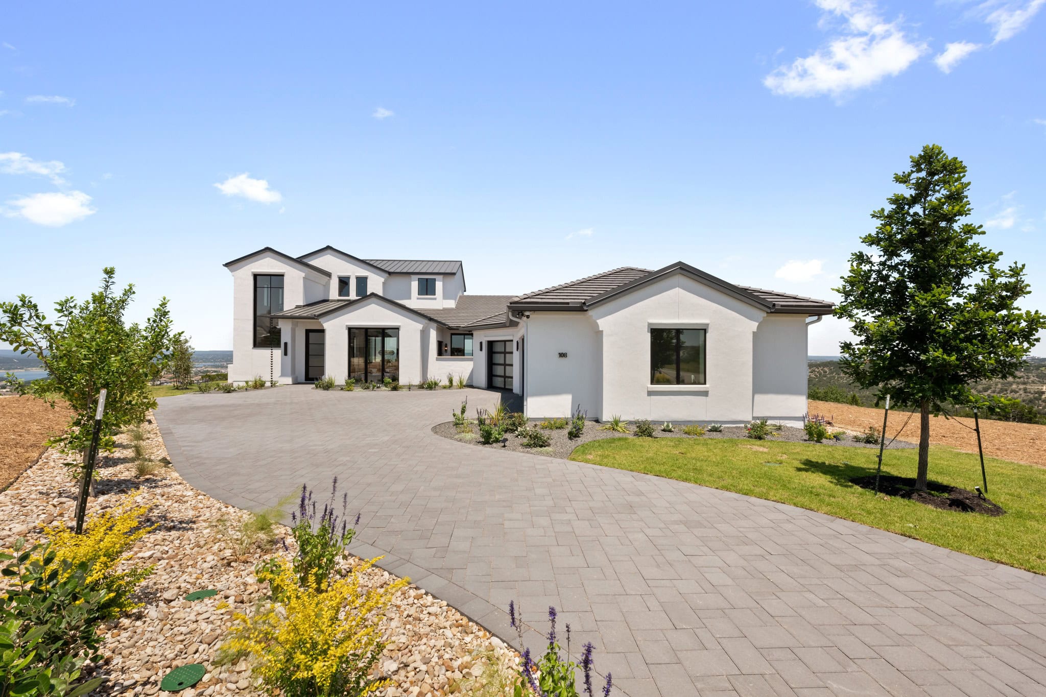 Hilltop Haven's exterior with a spacious paver driveway, landscaped front yard, and Hill Country views.