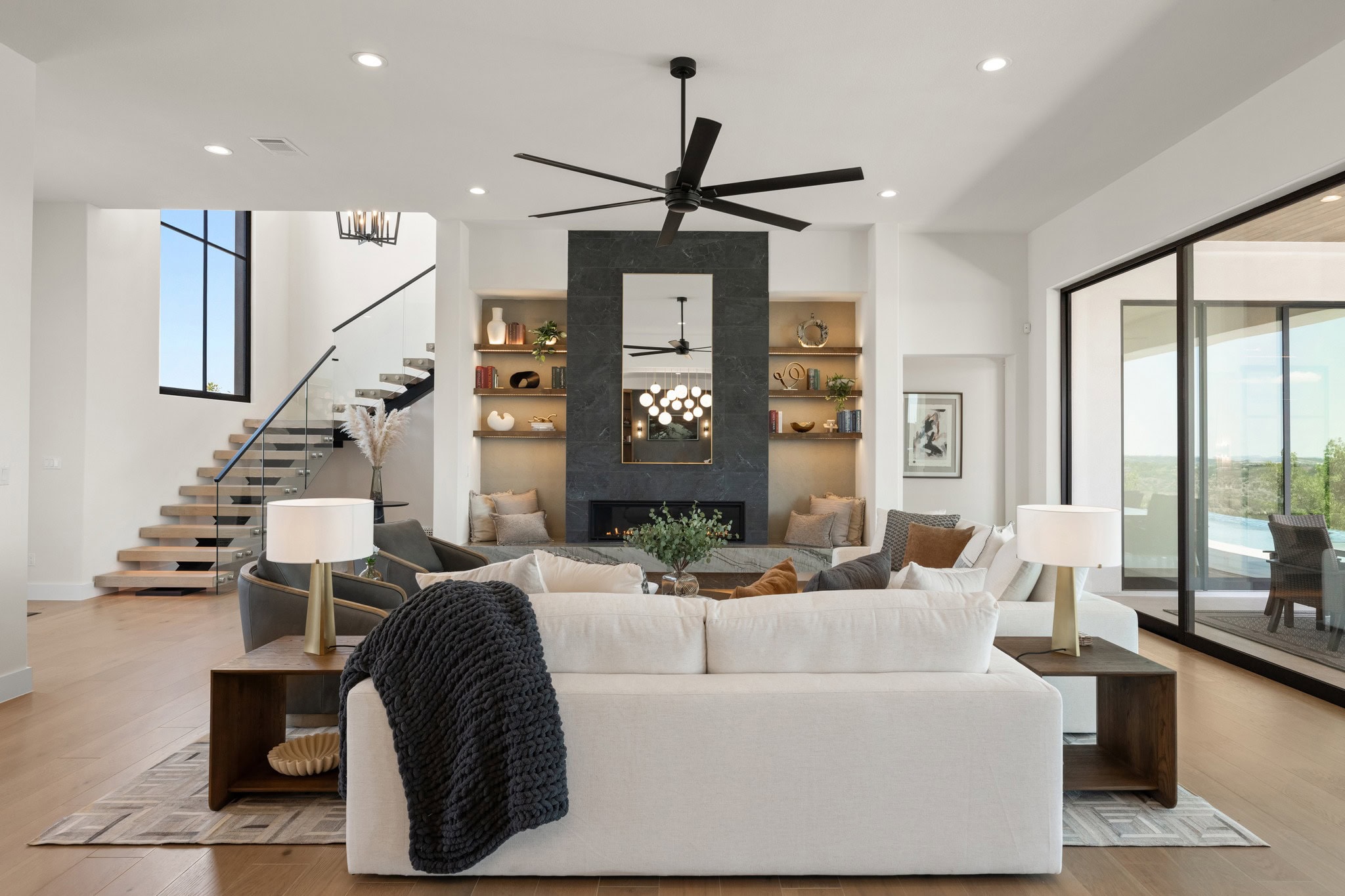 Hilltop Haven's luxury living room with a large fireplace, open staircase, and floor-to-ceiling glass doors overlooking the outdoors.